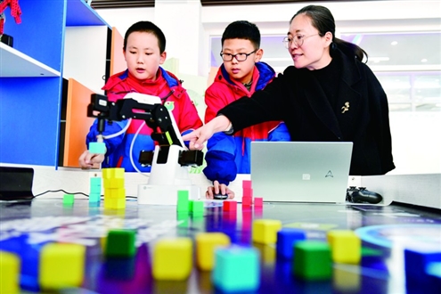 我省明年起将人工智能素养纳入学生综评。图为日照市新营小学老师指导学生使用人工智能机械臂。新华社发